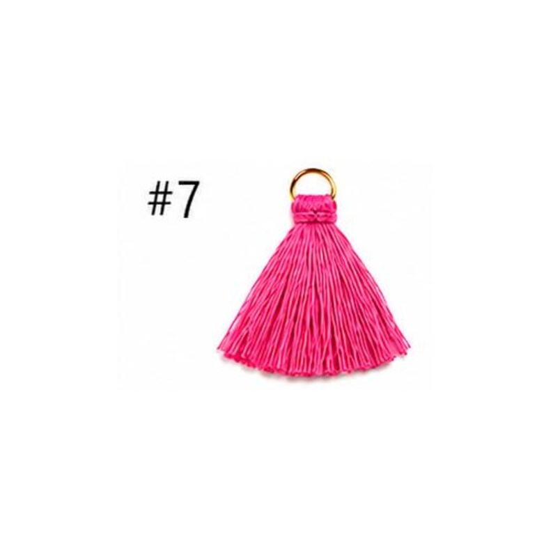 Peut inclure: Un pompon rose vif dot&eacute; d'un anneau en m&eacute;tal dor&eacute; sur le dessus pour la fixation. Le pompon est compos&eacute; de nombreux fils verticaux fins qui s'&eacute;vasent &agrave; partir d'une base nou&eacute;e centrale. Le texte #7 est visible sur la gauche.