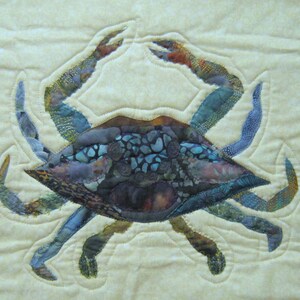 May include: A blue and brown patchwork fabric crab with a beige background. The crab is made of different fabrics and has a detailed design.