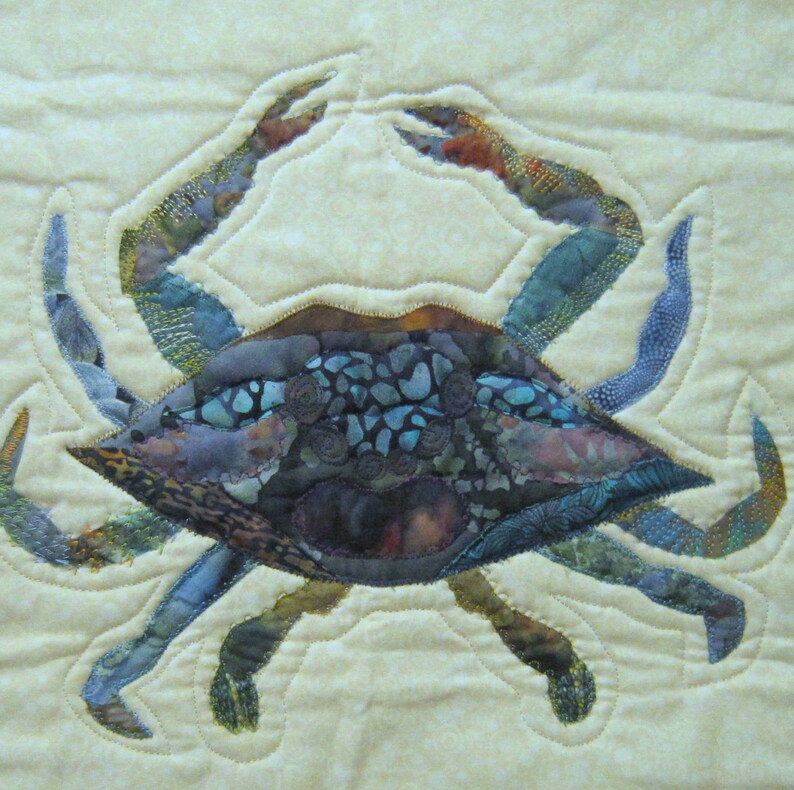 May include: A blue and brown patchwork fabric crab with a beige background. The crab is made of different fabrics and has a detailed design.