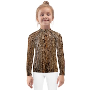 May include: A child wearing a long-sleeved shirt with a brown and tan tree bark pattern. The shirt has a mock neck and long sleeves.