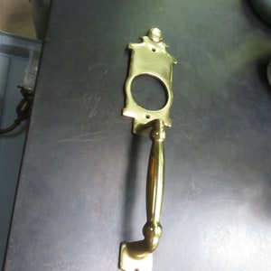 May include: A gold-toned door handle with a decorative plate and a long, curved handle.