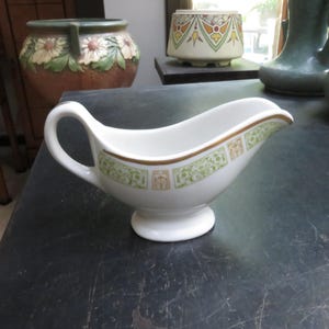 May include: A white ceramic gravy boat with a gold trim and green and brown floral design.