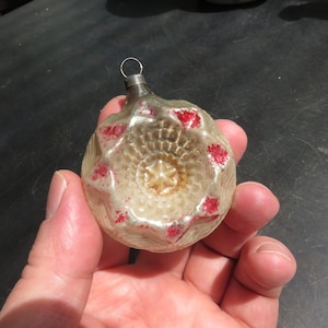 May include: A vintage glass Christmas ornament with a white and silver finish and red accents. The ornament has a star-shaped design and a textured surface.
