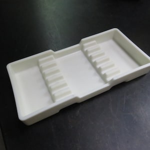 May include: A white plastic tray with two rows of indentations, designed for holding and organizing small items.