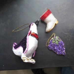 May include: Three beaded Christmas ornaments: a penguin with black and white sequins, a red and white boot, and a purple grape cluster.