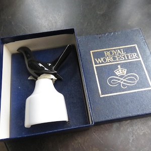 May include: A black and white ceramic bird figurine, presented in a blue box. The bird has a sleek, glossy finish and sits atop a white base. The box features the "Royal Worcester" logo in gold lettering, suggesting a collectible item.