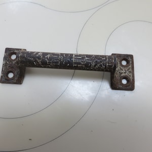 May include: A rusty metal door handle with a decorative design. The handle is brown with white paint accents.