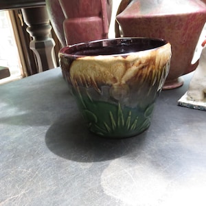 May include: A ceramic planter featuring a deep green base with embossed leaf patterns and a contrasting drip glaze in shades of cream and brown at the rim. The interior of the pot is finished in a dark, glossy brown glaze, creating a distinct color transition.