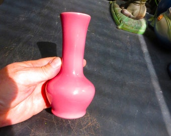 May include: A small, pink ceramic vase with a rounded base and a narrow neck. The vase is sitting on a dark surface.