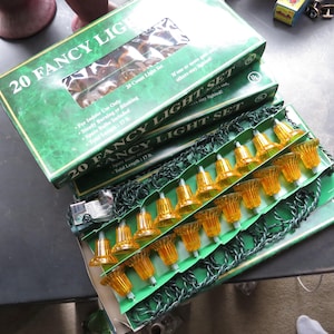 May include: A set of 20 fancy light set in a green box. The lights are shaped like bells and are amber in color. The box reads "20 Fancy Light Set" and "Total Length 17 ft."