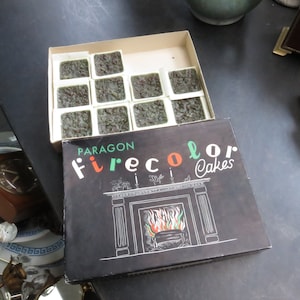 Puede incluir: Una caja de pasteles Firecolor Paragon, una marca de ingredientes para hornear de color verde. La caja presenta una ilustración en blanco y negro de una chimenea con fuego ardiendo en su interior. El texto "Paragon Firecolor Cakes" está impreso en la parte delantera de la caja.