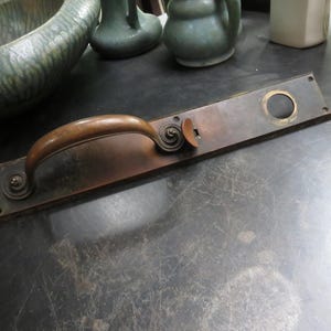 May include: Antique bronze door handle with a curved handle and rectangular backplate. The handle features decorative spiral detailing on each end and a keyhole. The bronze has a warm, aged patina, suggesting its vintage origin.