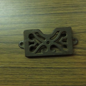 May include: A cast iron decorative vent cover with a floral design. The vent cover is dark brown and has a rectangular shape.