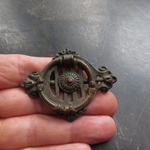 May include: Antique bronze cabinet door pull with ornate details and a decorative center. The pull has a ring-shaped handle and a decorative, openwork design.