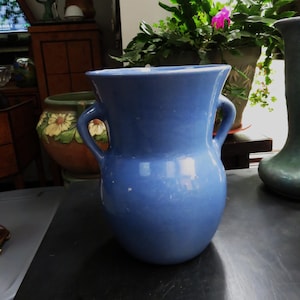 May include: A light blue ceramic vase with two handles. The vase has a rounded body and a slightly flared top.