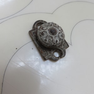 May include: A silver-toned metal latch with a decorative knob. The knob has a circular design with a raised centre and a textured surface.
