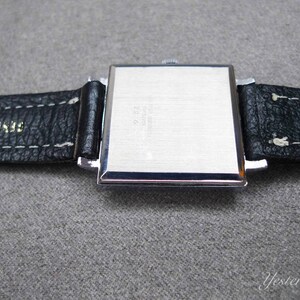 May include: A silver square watch with a black leather strap. The strap has white stitching and the text "Genuine Leather" is printed on the strap.
