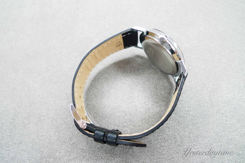 May include: A silver wristwatch with a black leather band. The watch face is not visible in the image.