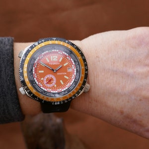 May include: A black and orange wristwatch with a rotating bezel and a world time dial. The watch face features the text "TE GROV AVIATION".