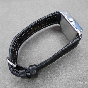 May include: A silver square-shaped wristwatch with a black leather band. The band is labeled "Genuine Leather" on the back.