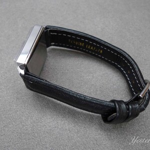 May include: A silver square watch with a black leather band. The band is stitched with white thread and has the words "Genuine Leather" printed on it.