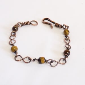 May include: A copper wire bracelet with tiger's eye beads. The bracelet has a clasp closure.