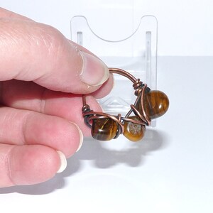 May include: A copper wire ring with three brown tiger's eye stones wrapped in the wire.
