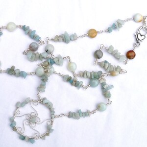 May include: A silver chain necklace with a circular pendant made of wire and aquamarine stones. The necklace is made with small, irregular aquamarine stones and a few larger round stones.