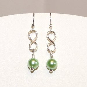 May include: Silver infinity symbol earrings with a light green pearl dangle.
