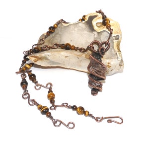 May include: A copper wire necklace with a spiral pendant and tiger's eye beads.