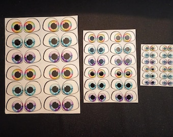 Peut inclure: Plusieurs feuilles d'autocollants en forme d'yeux de différentes tailles. Chaque autocollant présente un design d'œil détaillé avec une sclère blanche, un contour noir et un iris coloré. Les iris affichent une gamme de couleurs, dont le bleu, le violet, le jaune et les teintes arc-en-ciel.