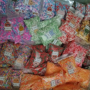 May include: A collection of clear plastic bags filled with colorful sprinkles. Each bag features a sticker with a cartoon bunny and a number. The sprinkles are in various colors, including pink, blue, green, red, and orange.