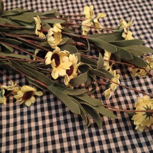 May include: A collection of artificial yellow sunflowers with brown centers and green leaves. The stems are brown and the flowers are arranged on a black and white checkered surface.