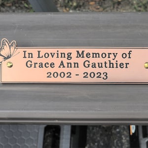 May include: A copper-colored memorial plaque with a butterfly design and the text "In Loving Memory of Grace Ann Gauthier 2002 - 2023".