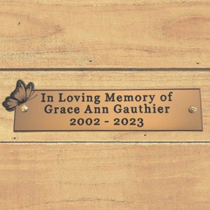 May include: A brass plaque with a butterfly design and the text "In Loving Memory of Grace Ann Gauthier 2002 - 2023".