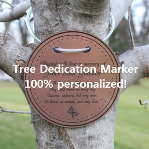May include: A round, copper-colored tree dedication marker with the text "Planted with love in memory of Grace Ann Gauthier. They walk beside us every day. Unseen, unheard, but very near. So loved, so missed, and very dear." and a butterfly design.