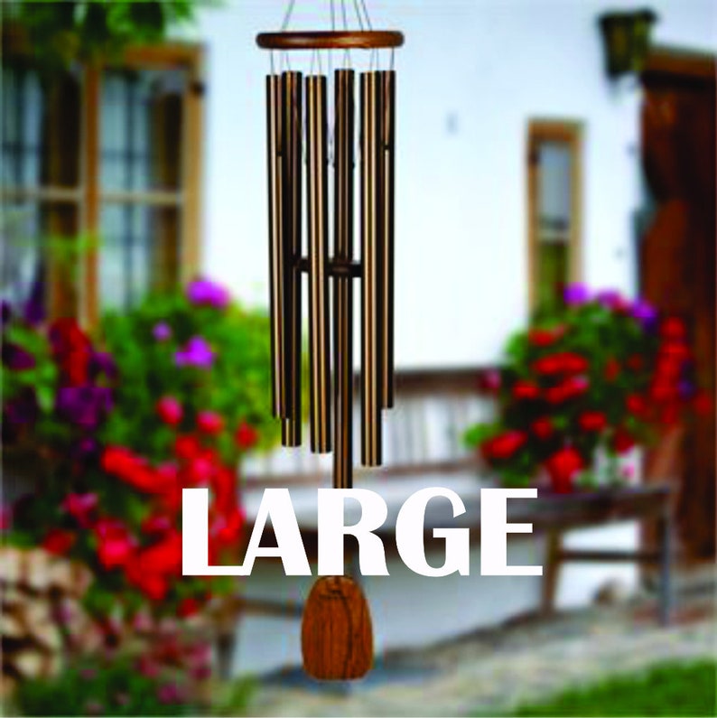 May include: A large, wooden wind chime with multiple metal tubes hanging from a wooden frame. The tubes are a mix of gold and brown tones. The wind chime is hanging outdoors in front of a window and flowers.