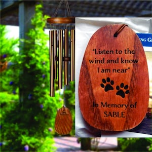May include: Wooden memorial wind chime with a brown oval-shaped plaque. The plaque has the text "Listen to the wind and know I am near" and two paw prints. Below the text is "In Memory of SABLE".