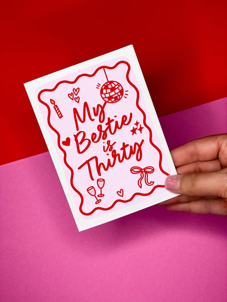 May include: A pink and white greeting card with red detailing. The card reads "My Bestie is Thirty" in a whimsical font, accompanied by illustrations of a disco ball, hearts, stars, a candle, and champagne glasses. The card is set against a red and pink backdrop.