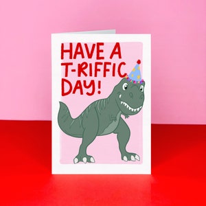 May include: A pink birthday card with a green dinosaur wearing a blue and yellow party hat. The card says "Have a T-riffic Day!"