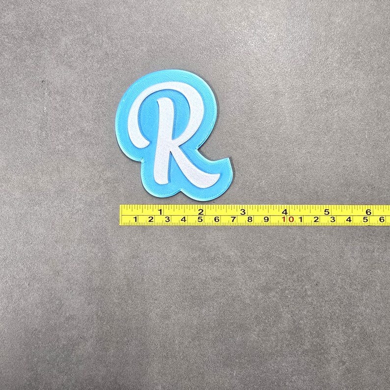 May include: A light blue felt letter R with a white outline. The letter is approximately 10 cm tall.