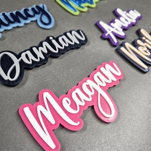 Puede incluir: Primer plano de varias etiquetas de nombre personalizadas. Los nombres están impresos en blanco sobre una variedad de fondos de colores. Los nombres incluyen Damian, Megan, Noelle, Andrew y Quincy.