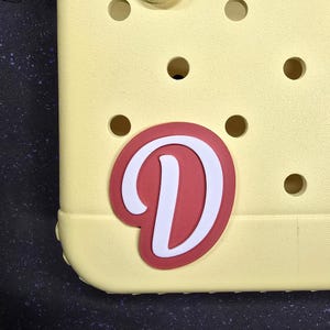 May include: A yellow plastic charm with a red and white letter D.
