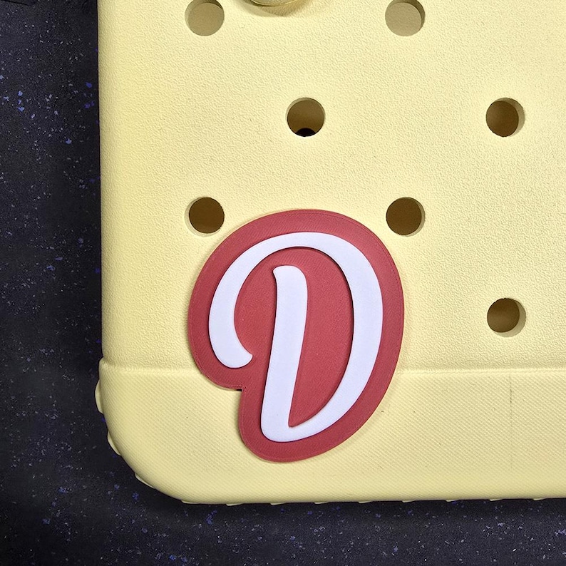 May include: A yellow plastic charm with a red and white letter D.