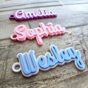 May include: Three layered name tags in the image. The top tag says "Amelia" in purple and white. The middle tag says "Sophia" in pink and white. The bottom tag says "Wesley" in blue and white.