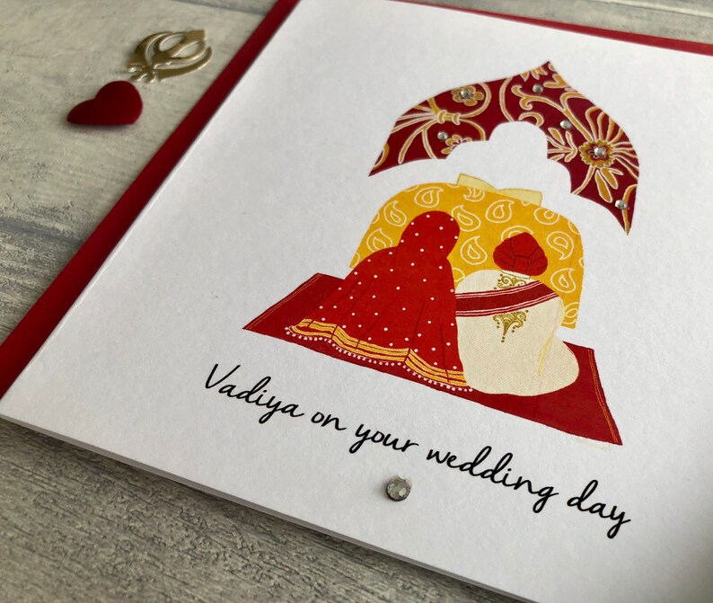 Close up view of the Anand Karaj Sikh wedding card. Illustration shows the Sikh couple sitting before the Guru Granth Sahib (Sikh Holy Book) Front is printed with, Vadiya (congratulations) on your wedding day.