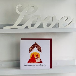 image shows a distant picture of the Anand Karaj Sikh wedding card. Illustration shows the Sikh couple sitting before the Guru Granth Sahib (Sikh Holy Book) for their Anand Karaj. Front is printed with, Congratulations on your wedding day and finished with diamanté.