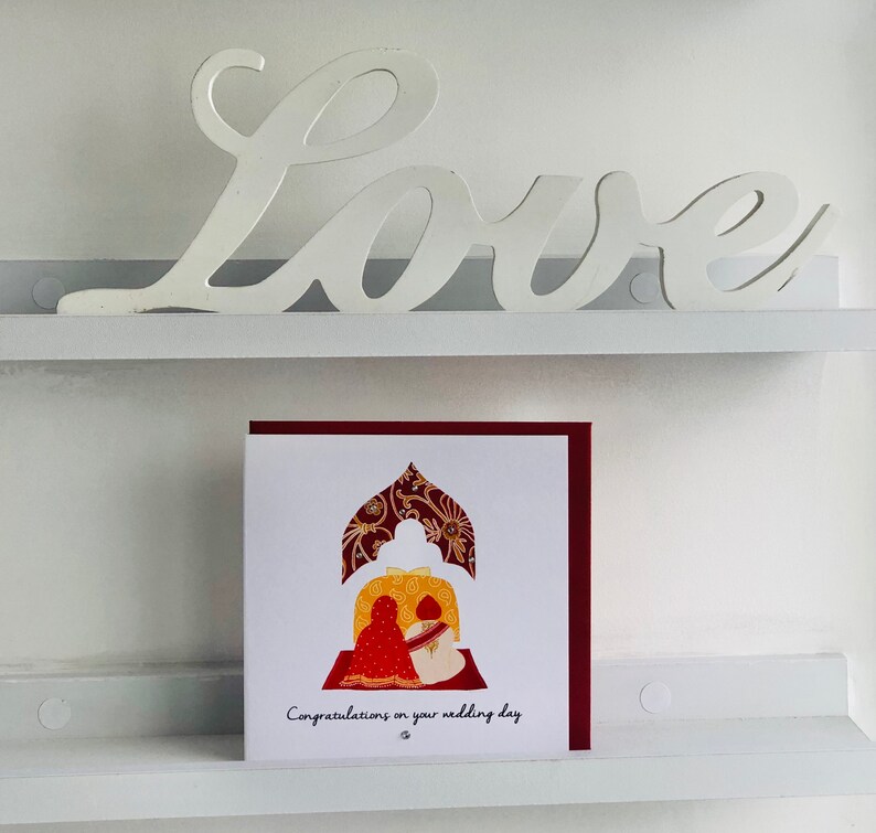image shows a distant picture of the Anand Karaj Sikh wedding card. Illustration shows the Sikh couple sitting before the Guru Granth Sahib (Sikh Holy Book) for their Anand Karaj. Front is printed with, Congratulations on your wedding day and finished with diamanté.