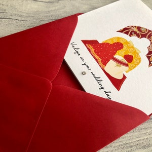 Anand Karaj Sikh wedding card is shown partially inside the red envelope. Illustration shows the Sikh couple sitting before the Guru Granth Sahib (Sikh Holy Book) Front is printed with, Vadiya on your wedding day.