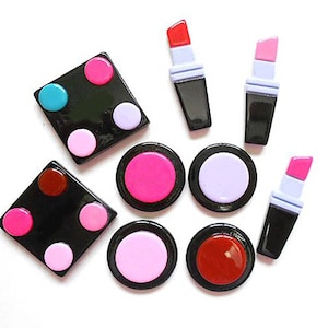 Puede incluir: Surtido de artículos de maquillaje coloridos, incluidos lápices labiales y paletas de sombras de ojos, en un diseño de lunares blanco y negro.